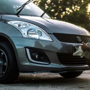 A man carefully cleans a car hood at sunset, focusing on details.